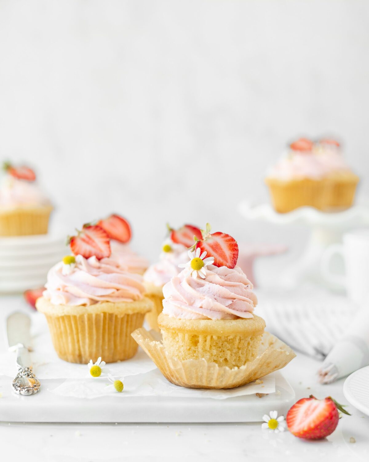 Gluten free strawberries and cream cupcakes styled on a marble serving board. They are topped with strawberries and camomile flowers.