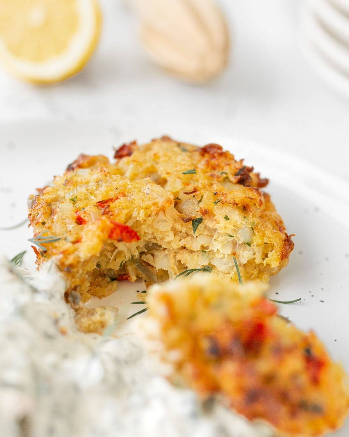 Air-fryer Cod Cakes with Tartar Sauce cut into on a plate (straight on, close-up)