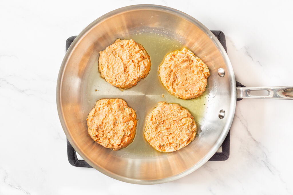 Process shot #5: Salmon and Sweet Potato Cakes formed and cooking in a stainless steel skillet with olive oil.