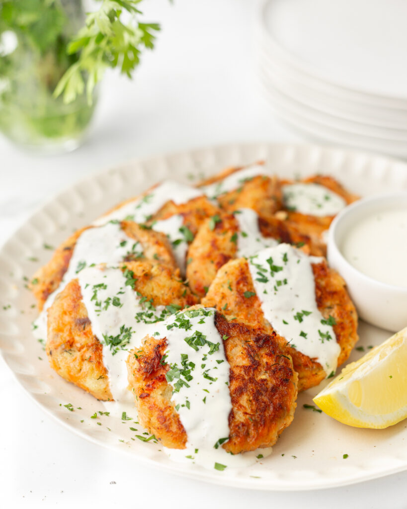 Salmon and Sweet Potato Cakes served on a plate and drizzled with lemon aioli and fresh parsley.