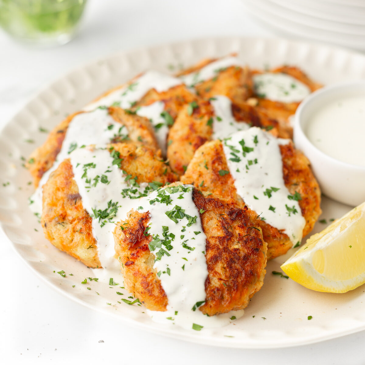 Salmon and sweet potato cakes plated and topped with lemon aioli and chopped fresh parsley.