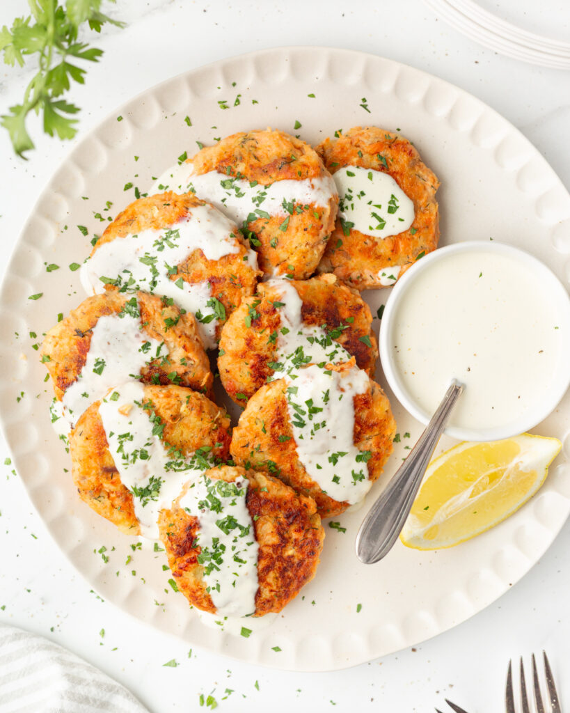 Salmon and sweet potato cakes plated with lemon aioli and fresh copped parsley sprinkled on top.