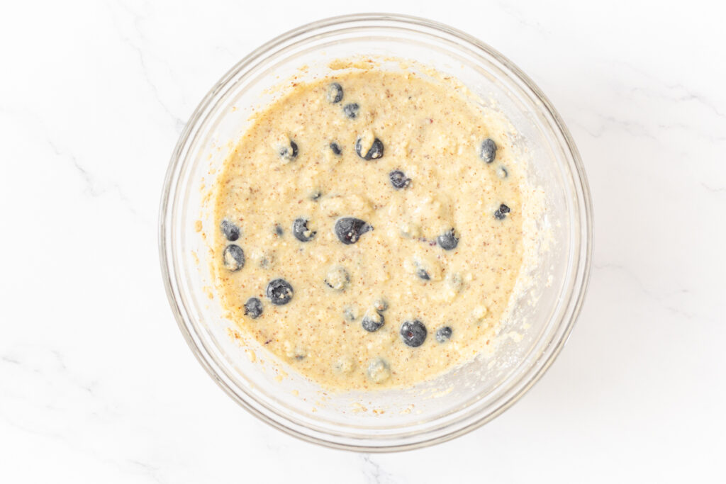 Process shot #3: Fresh blueberries mixed into the almond flour blueberry flax muffin batter in a glass mixing bowl. 