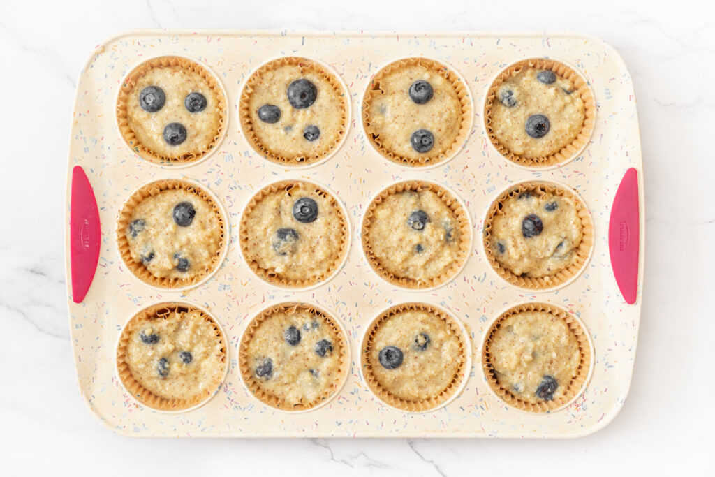 Process shot #4: Gluten Free Blueberry Muffin batter portioned into 12 paper liners in a silicone muffin tin. 