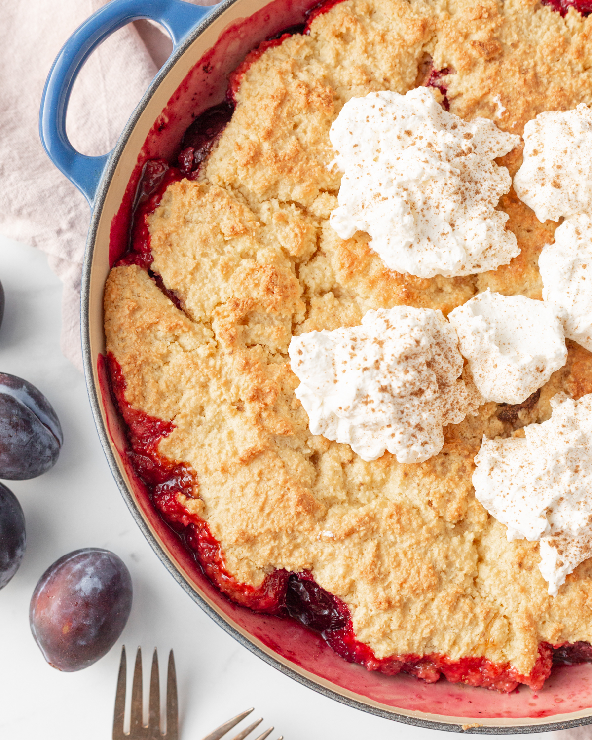 Gluten Free Prune Plum Cobbler baked in an enamelled cast iron skillet and topped with whipped cream.