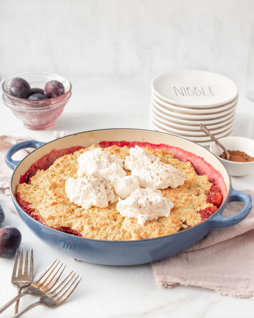 Gluten Free Prune Plum Cobbler baked in a round baking dish and topped with dollops of whipped cream. 