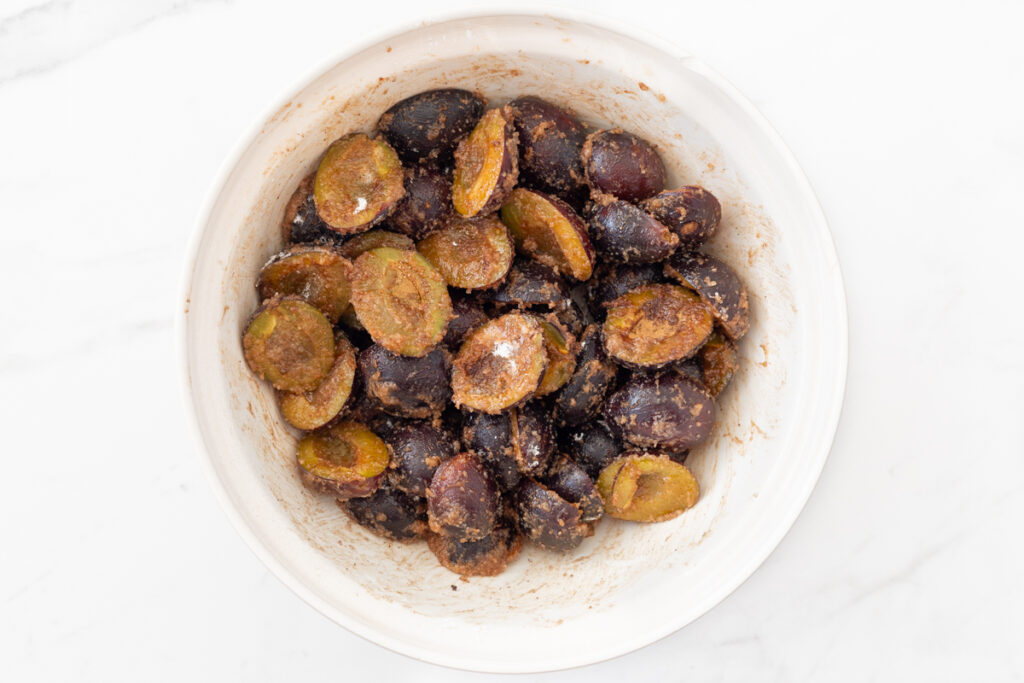 Process shot #1: Halved prune plums tossed with melted butter, sugar, lemon juice, cornstarch, cinnamon and cloves in a large mixing bowl.